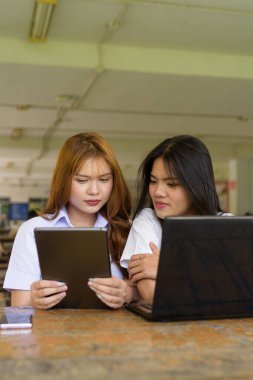 İki Taylandlı kız öğrenci açık havada bir üniversite kafesinde oturuyor. Arkadaşlık ya da çift sahnesi, gündelik yaşam tarzı, eğitim ve gençlik kültürü.