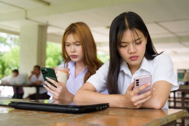 İki Taylandlı kız öğrenci açık havada bir üniversite kafesinde oturuyor. Arkadaşlık ya da çift sahnesi, gündelik yaşam tarzı, eğitim ve gençlik kültürü.