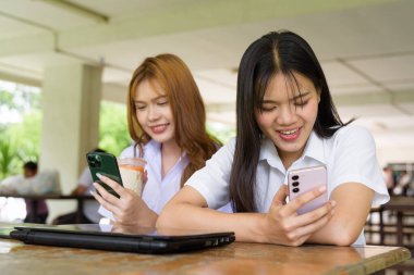 İki Taylandlı kız öğrenci açık havada bir üniversite kafesinde oturuyor. Arkadaşlık ya da çift sahnesi, gündelik yaşam tarzı, eğitim ve gençlik kültürü.