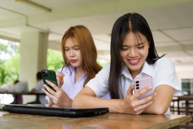 İki Taylandlı kız öğrenci açık havada bir üniversite kafesinde oturuyor. Arkadaşlık ya da çift sahnesi, gündelik yaşam tarzı, eğitim ve gençlik kültürü.
