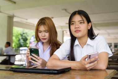 İki Taylandlı kız öğrenci açık havada bir üniversite kafesinde oturuyor. Arkadaşlık ya da çift sahnesi, gündelik yaşam tarzı, eğitim ve gençlik kültürü.