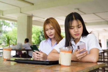 İki Taylandlı kız öğrenci açık havada bir üniversite kafesinde oturuyor. Arkadaşlık ya da çift sahnesi, gündelik yaşam tarzı, eğitim ve gençlik kültürü.