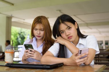 İki Taylandlı kız öğrenci açık havada bir üniversite kafesinde oturuyor. Arkadaşlık ya da çift sahnesi, gündelik yaşam tarzı, eğitim ve gençlik kültürü.