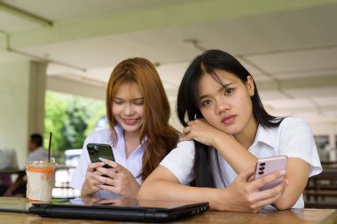 İki Taylandlı kız öğrenci açık havada bir üniversite kafesinde oturuyor. Arkadaşlık ya da çift sahnesi, gündelik yaşam tarzı, eğitim ve gençlik kültürü.