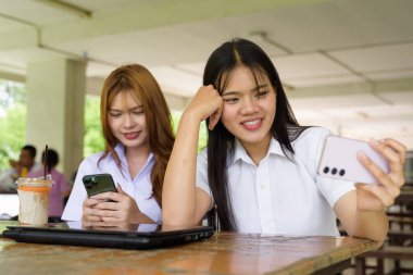 İki Taylandlı kız öğrenci açık havada bir üniversite kafesinde oturuyor. Arkadaşlık ya da çift sahnesi, gündelik yaşam tarzı, eğitim ve gençlik kültürü.