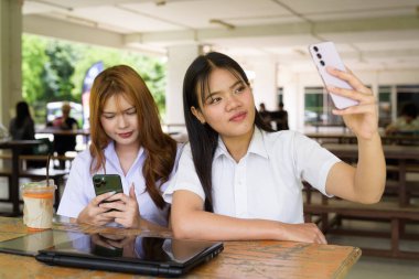 İki Taylandlı kız öğrenci açık havada bir üniversite kafesinde oturuyor. Arkadaşlık ya da çift sahnesi, gündelik yaşam tarzı, eğitim ve gençlik kültürü.