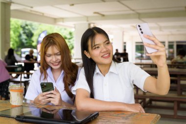İki Taylandlı kız öğrenci açık havada bir üniversite kafesinde oturuyor. Arkadaşlık ya da çift sahnesi, gündelik yaşam tarzı, eğitim ve gençlik kültürü.