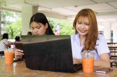 İki Taylandlı kız öğrenci açık havada bir üniversite kafesinde oturuyor. Arkadaşlık ya da çift sahnesi, gündelik yaşam tarzı, eğitim ve gençlik kültürü.