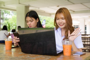 İki Taylandlı kız öğrenci açık havada bir üniversite kafesinde oturuyor. Arkadaşlık ya da çift sahnesi, gündelik yaşam tarzı, eğitim ve gençlik kültürü.