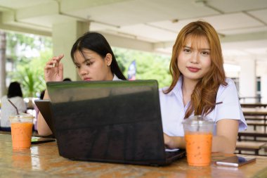 İki Taylandlı kız öğrenci açık havada bir üniversite kafesinde oturuyor. Arkadaşlık ya da çift sahnesi, gündelik yaşam tarzı, eğitim ve gençlik kültürü.