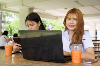 İki Taylandlı kız öğrenci açık havada bir üniversite kafesinde oturuyor. Arkadaşlık ya da çift sahnesi, gündelik yaşam tarzı, eğitim ve gençlik kültürü.