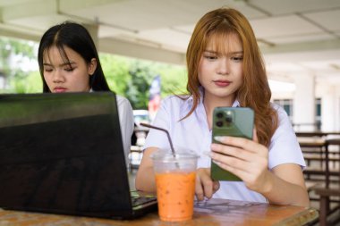 İki Taylandlı kız öğrenci açık havada bir üniversite kafesinde oturuyor. Arkadaşlık ya da çift sahnesi, gündelik yaşam tarzı, eğitim ve gençlik kültürü.