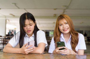 İki Taylandlı kız öğrenci açık havada bir üniversite kafesinde oturuyor. Arkadaşlık ya da çift sahnesi, gündelik yaşam tarzı, eğitim ve gençlik kültürü.