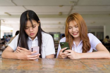 İki Taylandlı kız öğrenci açık havada bir üniversite kafesinde oturuyor. Arkadaşlık ya da çift sahnesi, gündelik yaşam tarzı, eğitim ve gençlik kültürü.