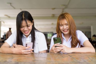 İki Taylandlı kız öğrenci açık havada bir üniversite kafesinde oturuyor. Arkadaşlık ya da çift sahnesi, gündelik yaşam tarzı, eğitim ve gençlik kültürü.