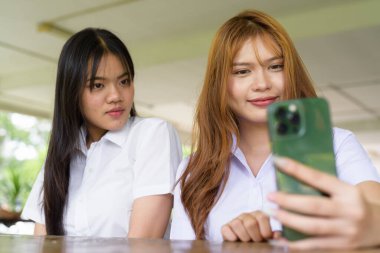 İki Taylandlı kız öğrenci açık havada bir üniversite kafesinde oturuyor. Arkadaşlık ya da çift sahnesi, gündelik yaşam tarzı, eğitim ve gençlik kültürü.