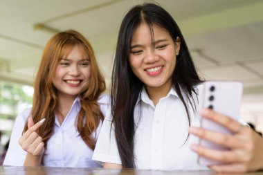 İki Taylandlı kız öğrenci açık havada bir üniversite kafesinde oturuyor. Arkadaşlık ya da çift sahnesi, gündelik yaşam tarzı, eğitim ve gençlik kültürü.