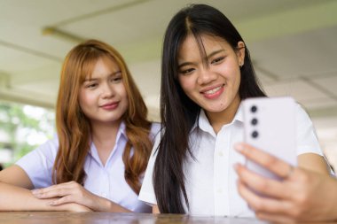 İki Taylandlı kız öğrenci açık havada bir üniversite kafesinde oturuyor. Arkadaşlık ya da çift sahnesi, gündelik yaşam tarzı, eğitim ve gençlik kültürü.