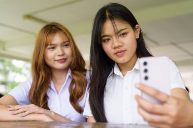 İki Taylandlı kız öğrenci açık havada bir üniversite kafesinde oturuyor. Arkadaşlık ya da çift sahnesi, gündelik yaşam tarzı, eğitim ve gençlik kültürü.