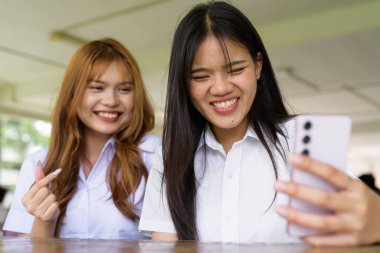 İki Taylandlı kız öğrenci açık havada bir üniversite kafesinde oturuyor. Arkadaşlık ya da çift sahnesi, gündelik yaşam tarzı, eğitim ve gençlik kültürü.