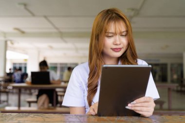 Üniversite üniformalı Taylandlı genç kız kampüsün kahve dükkanında tek başına oturuyor. Eğitimsel bir ortamda gerçek öğrenci hayatını, güzelliğini ve gençliğini gösteren rahat bir yaşam tarzı portresi..