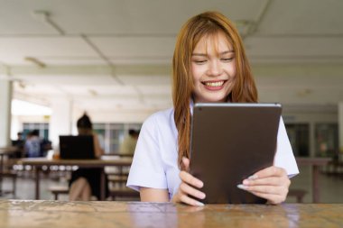 Üniversite üniformalı Taylandlı genç kız kampüsün kahve dükkanında tek başına oturuyor. Eğitimsel bir ortamda gerçek öğrenci hayatını, güzelliğini ve gençliğini gösteren rahat bir yaşam tarzı portresi..