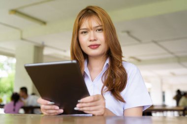 Üniversite üniformalı Taylandlı genç kız kampüsün kahve dükkanında tek başına oturuyor. Eğitimsel bir ortamda gerçek öğrenci hayatını, güzelliğini ve gençliğini gösteren rahat bir yaşam tarzı portresi..