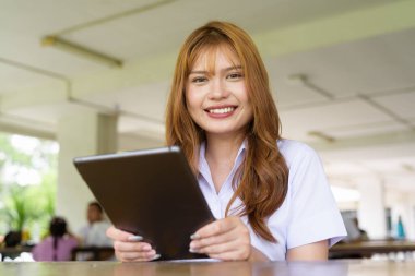 Üniversite üniformalı Taylandlı genç kız kampüsün kahve dükkanında tek başına oturuyor. Eğitimsel bir ortamda gerçek öğrenci hayatını, güzelliğini ve gençliğini gösteren rahat bir yaşam tarzı portresi..