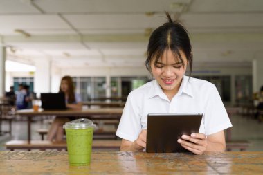 Üniversite üniformalı Taylandlı genç kız kampüsün kahve dükkanında tek başına oturuyor. Eğitimsel bir ortamda gerçek öğrenci hayatını, güzelliğini ve gençliğini gösteren rahat bir yaşam tarzı portresi..