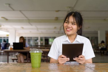 Üniversite üniformalı Taylandlı genç kız kampüsün kahve dükkanında tek başına oturuyor. Eğitimsel bir ortamda gerçek öğrenci hayatını, güzelliğini ve gençliğini gösteren rahat bir yaşam tarzı portresi..