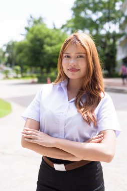 Güzel Tayland üniversitesi öğrencisi kampüste tek başına duruyor ve resmi akademik üniforma giyiyor. Gençlik, bağımsızlık ve akademik hırs odaklı otantik, modern eğitim teması.