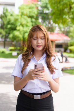 Güzel Tayland üniversitesi öğrencisi kampüste tek başına duruyor ve resmi akademik üniforma giyiyor. Gençlik, bağımsızlık ve akademik hırs odaklı otantik, modern eğitim teması.