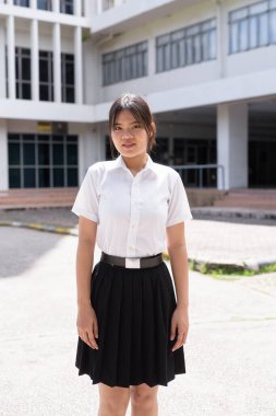 Güzel Tayland üniversitesi öğrencisi kampüste tek başına duruyor ve resmi akademik üniforma giyiyor. Gençlik, bağımsızlık ve akademik hırs odaklı otantik, modern eğitim teması.
