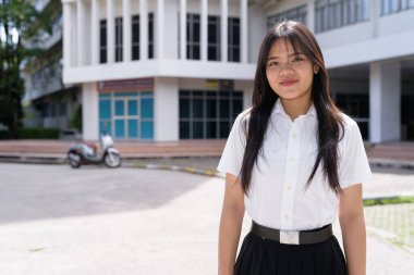Güzel Tayland üniversitesi öğrencisi kampüste tek başına duruyor ve resmi akademik üniforma giyiyor. Gençlik, bağımsızlık ve akademik hırs odaklı otantik, modern eğitim teması.