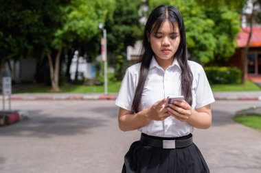 Güzel Tayland üniversitesi öğrencisi kampüste tek başına duruyor ve resmi akademik üniforma giyiyor. Gençlik, bağımsızlık ve akademik hırs odaklı otantik, modern eğitim teması.