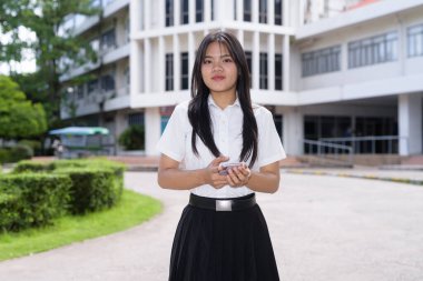 Güzel Tayland üniversitesi öğrencisi kampüste tek başına duruyor ve resmi akademik üniforma giyiyor. Gençlik, bağımsızlık ve akademik hırs odaklı otantik, modern eğitim teması.