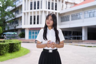 Güzel Tayland üniversitesi öğrencisi kampüste tek başına duruyor ve resmi akademik üniforma giyiyor. Gençlik, bağımsızlık ve akademik hırs odaklı otantik, modern eğitim teması.