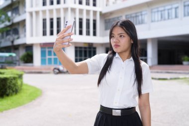 Güzel Tayland üniversitesi öğrencisi kampüste tek başına duruyor ve resmi akademik üniforma giyiyor. Gençlik, bağımsızlık ve akademik hırs odaklı otantik, modern eğitim teması.