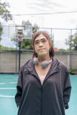 Açık hava basketbol sahasında duran fit bir transseksüel kadının portresi. Güç ve kentsel fitness yaşam tarzını destekliyor.