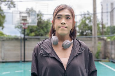 Açık hava basketbol sahasında duran fit bir transseksüel kadının portresi. Güç ve kentsel fitness yaşam tarzını destekliyor.