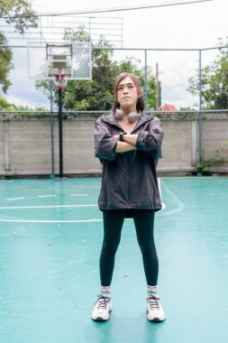 Açık hava basketbol sahasında duran fit bir transseksüel kadının portresi. Güç ve kentsel fitness yaşam tarzını destekliyor.