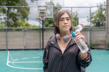 Açık hava basketbol sahasında duran fit bir transseksüel kadının portresi. Güç ve kentsel fitness yaşam tarzını destekliyor.