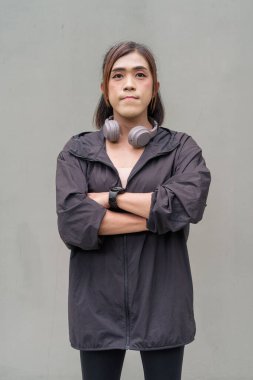 Açık hava duvarının önünde spor kıyafetler giymiş transseksüel bir Asyalı kadının portresi.