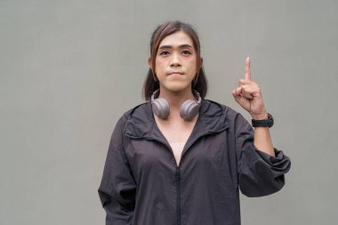 Açık hava duvarının önünde spor kıyafetler giymiş transseksüel bir Asyalı kadının portresi.