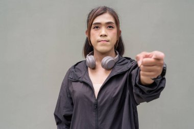 Açık hava duvarının önünde spor kıyafetler giymiş transseksüel bir Asyalı kadının portresi.