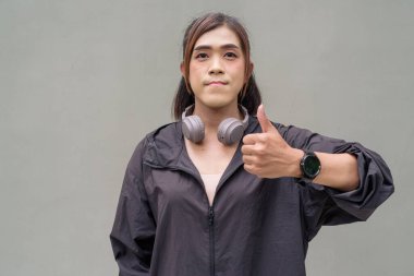 Açık hava duvarının önünde spor kıyafetler giymiş transseksüel bir Asyalı kadının portresi.