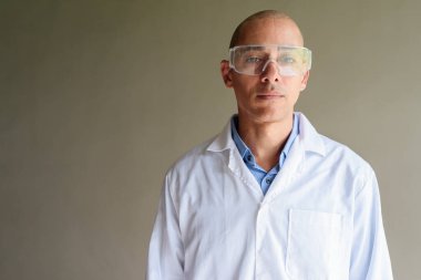 Beyaz önlüklü ve koruyucu gözlüklü, düz duvara poz veren kendinden emin bir bilim adamı. Stüdyo bilimi konsepti.
