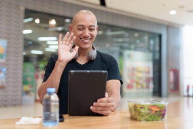 Normal ortamlarda dijital tablet bilgisayar ve salata kullanan sağlıklı yetişkin bir adam. Gıda mahkemelerinde teknoloji, beslenme ve modern yaşam tarzı arasındaki dengeyi vurgular.