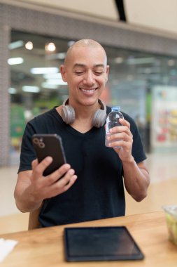 Normal ortamlarda dijital tablet bilgisayar ve salata kullanan sağlıklı yetişkin bir adam. Gıda mahkemelerinde teknoloji, beslenme ve modern yaşam tarzı arasındaki dengeyi vurgular.