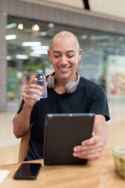 Normal ortamlarda dijital tablet bilgisayar ve salata kullanan sağlıklı yetişkin bir adam. Gıda mahkemelerinde teknoloji, beslenme ve modern yaşam tarzı arasındaki dengeyi vurgular.